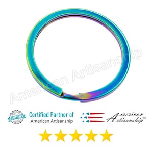 May include: A circular metal split ring featuring an iridescent rainbow finish with shifting hues of blue, green, and purple. The text American Artisanship is overlaid across the center, with a certification badge and five yellow stars below.