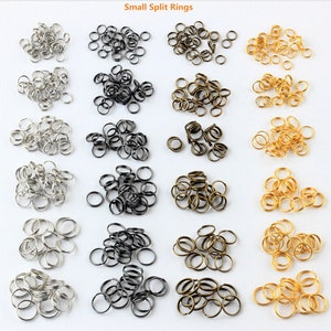 May include: A collection of small split rings in silver, black, and gold. The rings are arranged in rows of three, with each row containing a different color.