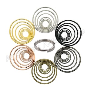 May include: Assortment of metal key rings in various sizes and finishes, including gold, silver, black, bronze, and rose gold. The key rings are arranged in a circle.