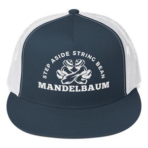 May include: A navy blue and white trucker hat with the text "STEP ASIDE STRING BEAN MANDELBAUM" in white. The hat features a white mesh back and a curved brim. The design includes a graphic of two crossed dumbbells.