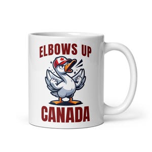 May include: White ceramic coffee mug with a cartoon goose wearing a Canadian flag hat and the text "Elbows Up Canada".