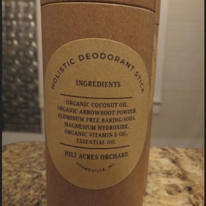 May include: A brown cardboard tube with a white label that reads "HOLISTIC DEODORANT STICK" and lists the ingredients: "ORGANIC COCONUT OIL, ORGANIC ARROWROOT POWDER, ALUMINUM FREE BAKING SODA, MAGNESIUM HYDROXIDE, ORGANIC VITAMIN E OIL, ESSENTIAL OIL". The label also includes the company name "HILI ACRES ORCHARD" and the location "STONEVILLE, NC."