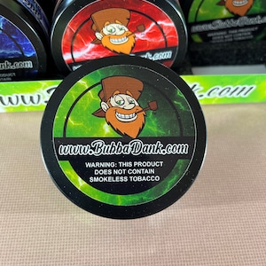 May include: A green and black round container with a cartoon character on the front. The character is wearing a brown hat and has a beard. The text on the container reads "www.BubbaDank.com" and "WARNING: THIS PRODUCT DOES NOT CONTAIN SMOKELESS TOBACCO".