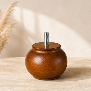 May include: A round, dark brown wooden furniture leg with a smooth, polished finish. The top of the leg features a flat surface with a centered, silver-colored metal threaded bolt extending upwards for attachment to a furniture base.