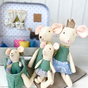 May include: Four handmade fabric mouse dolls with pink ears and smiling faces. The mice wear green dresses and some have gold crowns. One mouse is in a green pouch. A suitcase with curtains is in the background.