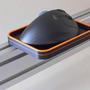 May include: A black ergonomic mouse with an orange trim sits on a black and orange tray. The tray is mounted on a silver track.