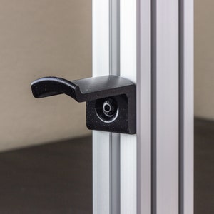 May include: A black plastic handle with a silver metal frame. The handle is attached to a door or cabinet.