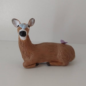 May include: A brown clay deer figurine with blue eyes and a purple butterfly on its back.