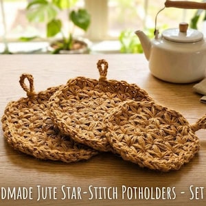 May include: Three handmade jute star-stitch potholders with a natural, woven texture. Each round potholder has a loop for hanging. A white teapot with a wooden handle sits in the background on a wooden table.