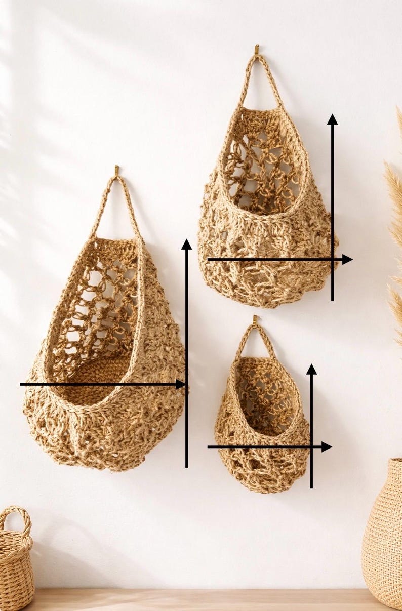 May include: Three woven jute hanging baskets of different sizes, suspended from brass hooks on a white wall. The baskets have open, textured weaves and a natural, light brown colour, suitable for storage or decoration.