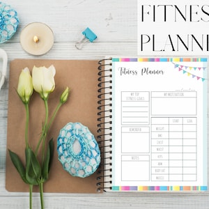 Könnte beinhalten: Ein Fitness-Planer mit einem blauen und weißen Cover. Der Planer hat Abschnitte zum Setzen von Fitnesszielen, zur Verfolgung des Fortschritts und zum Schreiben von Notizen. Der Planer ist auf einer Seite geöffnet, die eine Tabelle zum Verfolgen von Gewicht, BMI, Brustumfang, Taille, Hüfte, Arm, Körperfett und Muskeln enthält.