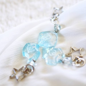 Puede incluir: Un brazalete de plata con dijes de vidrio azul en forma de casas y un dije de estrella. Los dijes están decorados con brillantina.