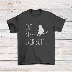 May include: A dark gray t-shirt with a white cat illustration and the text "EAT. SLEEP. LICK BUTT."