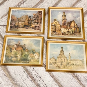 Peut inclure: Quatre impressions encadrées à l'aquarelle représentant des paysages urbains européens. Chaque impression est dans un cadre doré. Les paysages urbains représentent des bâtiments, des rues et des détails architecturaux.
