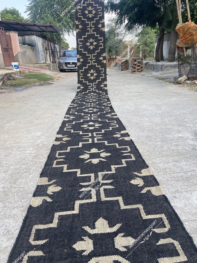 May include: Black and white geometric patterned rug with a woven texture. The rug is laid out on a paved surface.