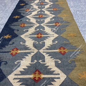 May include: A long, narrow rug with a geometric pattern in shades of blue, beige, and brown. The rug has a traditional, tribal design with repeating motifs.