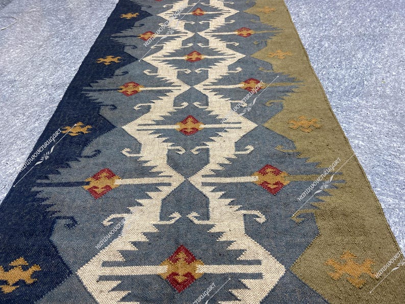 May include: A long, narrow rug with a geometric pattern in shades of blue, beige, and brown. The rug has a traditional, tribal design with repeating motifs.