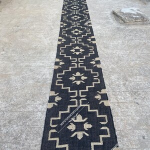 May include: Black and white geometric patterned rug with fringe on the ends. The rug is made of natural fibers and has a rustic look.