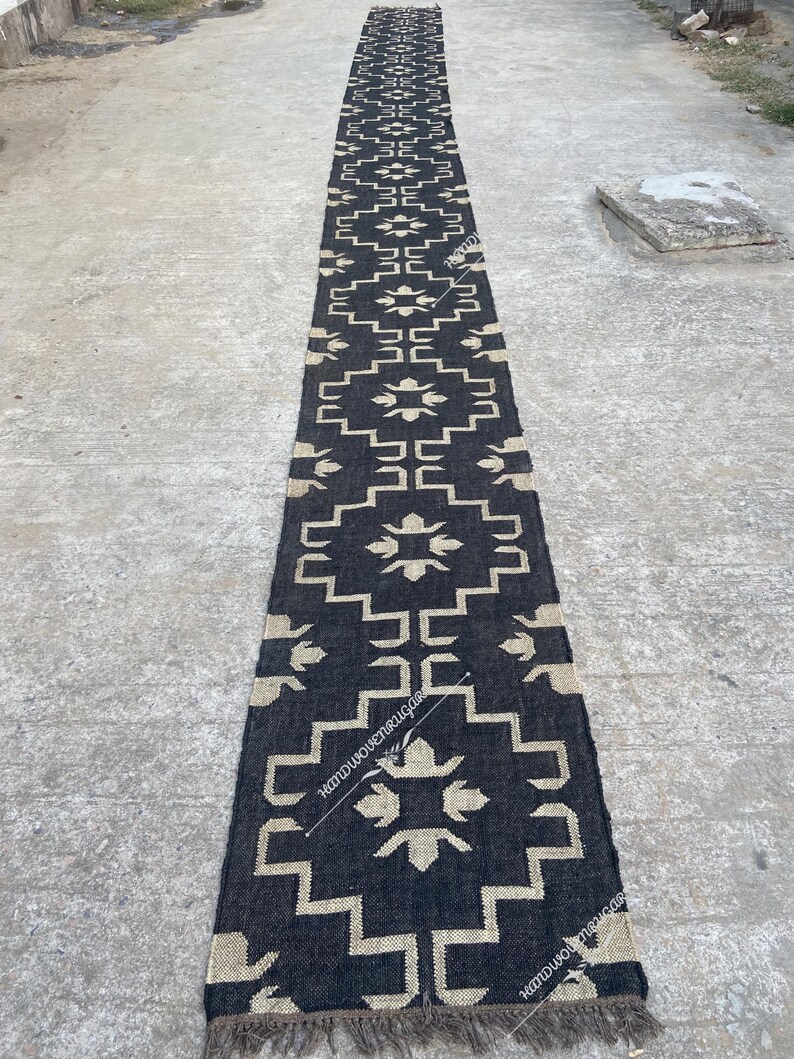 May include: Black and white geometric patterned rug with fringe on the ends. The rug is made of natural fibers and has a rustic look.