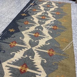 May include: A long, rectangular rug with a geometric pattern in shades of gray, white, brown, and red. The rug has a traditional, tribal design.