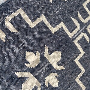 May include: Black and white geometric patterned rug with a woven texture. The rug features a repeating pattern of stylized leaves and zigzags.