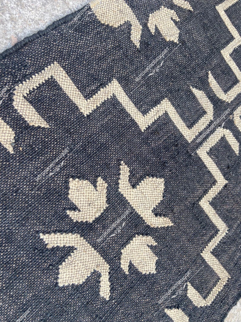 May include: Black and white geometric patterned rug with a woven texture. The rug features a repeating pattern of stylized leaves and zigzags.
