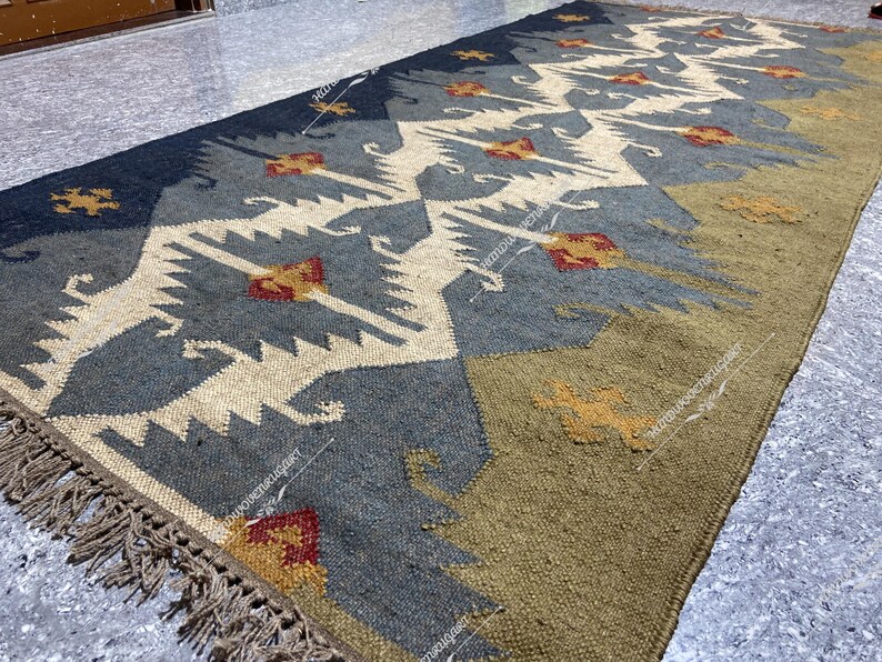 May include: A handwoven rug with a geometric pattern in shades of blue, beige, and brown. The rug has a fringe border and is made of natural fibers.
