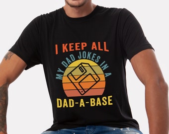 May include: A black t-shirt with a retro-style graphic of a floppy disk and the text "I keep all my dad jokes in a dad-a-base".