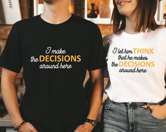Könnte beinhalten: Zwei T-Shirts, eines schwarz und eines weiß, mit passendem Text. Das schwarze Shirt trägt den Schriftzug "I make the DECISIONS around here" in weiß und gold. Das weiße Shirt trägt "I let him THINK that he makes the DECISIONS around here."