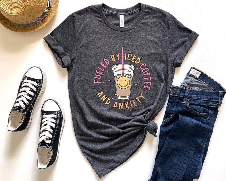 May include: A dark gray t-shirt with a graphic of a cup of iced coffee with a smiley face and the text "Fueled by Iced Coffee and Anxiety".