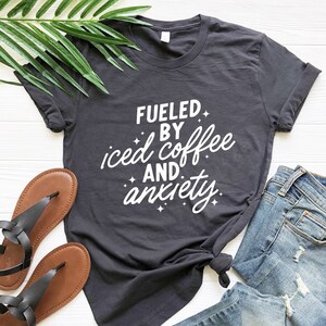May include: A dark gray t-shirt with white text that reads "Fueled by iced coffee and anxiety".