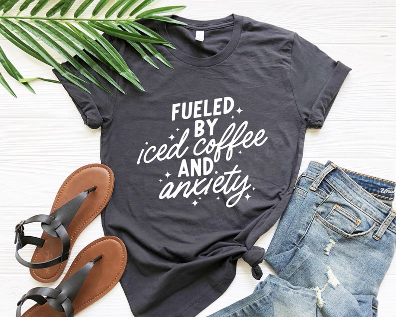May include: A dark gray t-shirt with white text that reads "Fueled by iced coffee and anxiety".