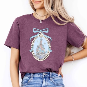 Puede incluir: Una camiseta morada con un gr&aacute;fico de un castillo en un marco de perlas y una cinta azul.