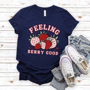 May include: A navy blue t-shirt with a graphic of strawberries and the text "Feeling Berry Good".