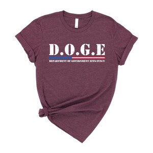 May include: A maroon t-shirt with a white graphic that says "D.O.G.E. DEPARTMENT OF GOVERNMENT EFFICIENCY" with a red, white, and blue stripe underneath.