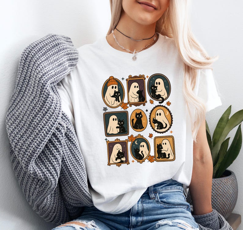 Puede incluir: Camiseta blanca con un dise&ntilde;o tem&aacute;tico de Halloween. El gr&aacute;fico incluye ilustraciones enmarcadas de fantasmas y gatos negros, con hojas de oto&ntilde;o y una paleta de colores c&aacute;lidos. Una prenda casual para el d&iacute;a a d&iacute;a.