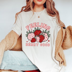 May include: A white t-shirt with a pink and red graphic of strawberries and the text "Feeling Berry Good".