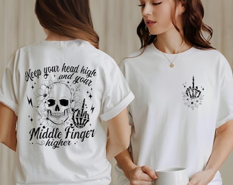 May include: White t-shirt with a black skull and middle finger design on the back. The front of the shirt has a smaller black middle finger design with flowers.