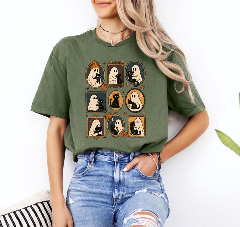 Puede incluir: Camiseta verde oliva con un gr&aacute;fico enmarcado de fantasmas y gatos negros. El dise&ntilde;o incluye fantasmas con sombreros y sosteniendo gatos, con hojas de oto&ntilde;o y detalles de luna. La camiseta es de estilo casual.