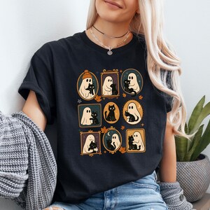 Puede incluir: Camiseta negra con ilustraciones enmarcadas de fantasmas y gatos negros. Las ilustraciones est&aacute;n en marcos ovalados y rectangulares con hojas de oto&ntilde;o. La camiseta tiene mangas cortas.