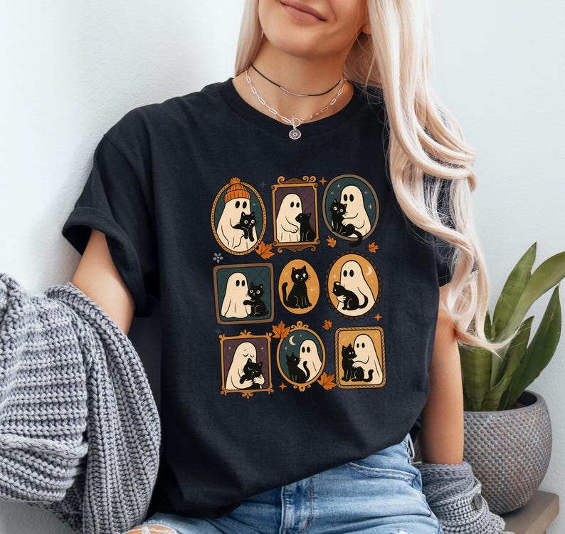 Puede incluir: Camiseta negra con ilustraciones enmarcadas de fantasmas y gatos negros. Las ilustraciones est&aacute;n en marcos ovalados y rectangulares con hojas de oto&ntilde;o. La camiseta tiene mangas cortas.