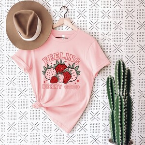 May include: Pink t-shirt with a graphic of strawberries and the text "Feeling Berry Good".