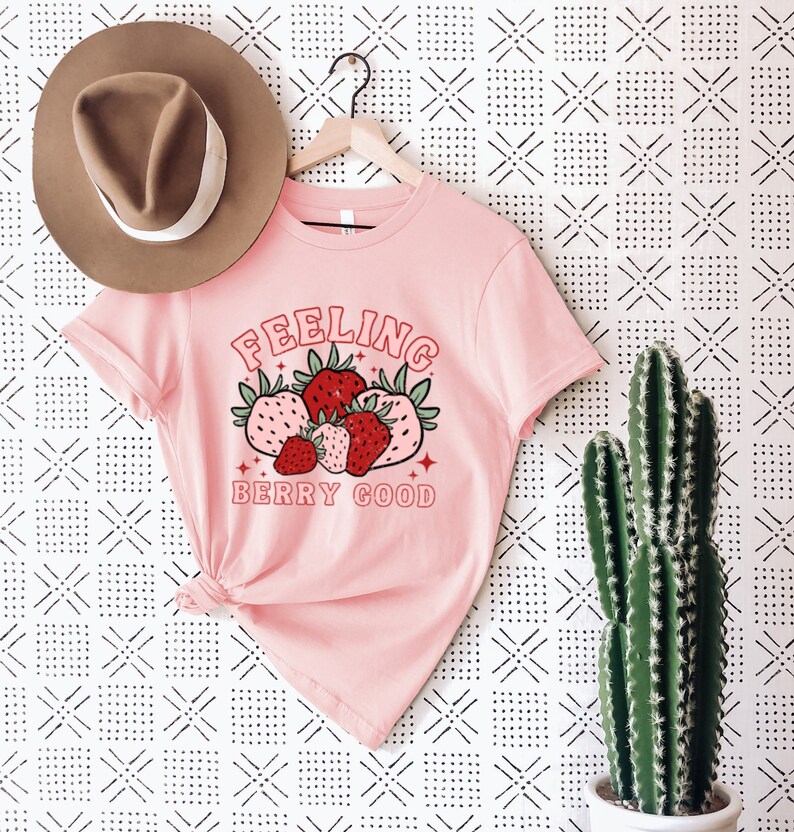 May include: Pink t-shirt with a graphic of strawberries and the text "Feeling Berry Good".