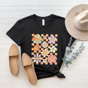 May include: Black t-shirt with a checkered pattern featuring colorful flowers with smiley faces.
