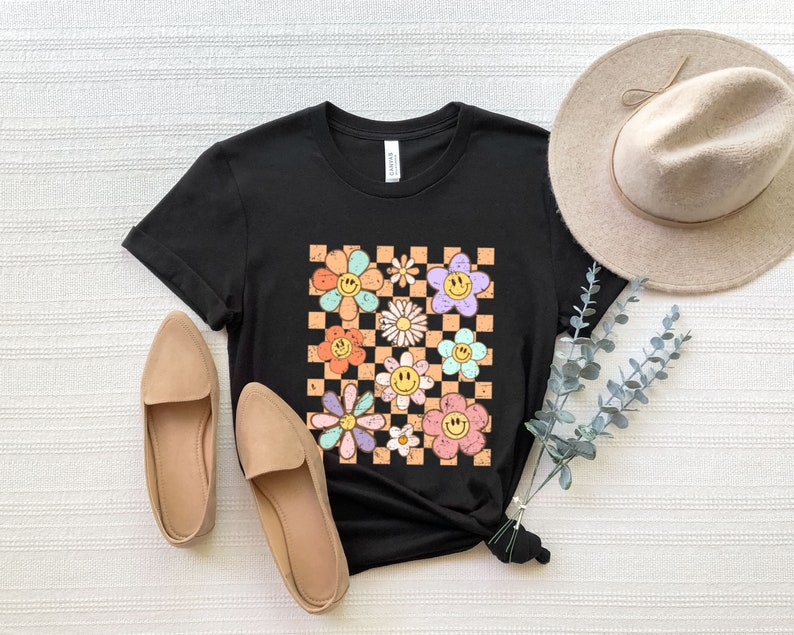 May include: Black t-shirt with a checkered pattern featuring colorful flowers with smiley faces.
