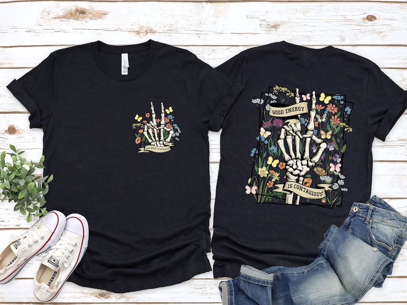May include: Two black t-shirts featuring a skeleton hand graphic and floral design. The front shirt has a smaller graphic with the text "Good Energy is Contagious". The back shirt has a larger graphic with the text "Good Energy is Contagious".