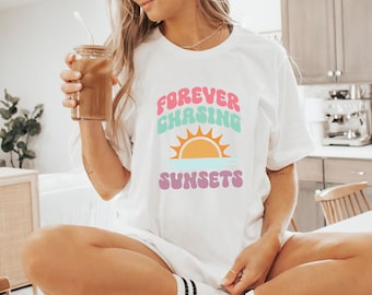 May include: A white t-shirt with a graphic design that says "FOREVER CHASING SUNSETS" in a retro font with a colorful sunset graphic.