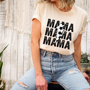 May include: A cream colored t-shirt with a black graphic of a lightning bolt made of soccer balls and the word "MAMA" repeated three times.