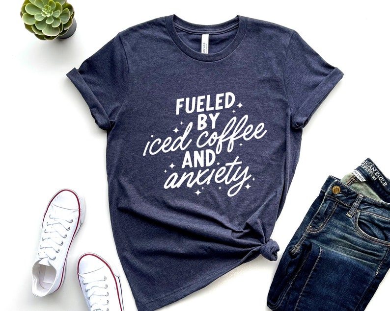 May include: A navy blue t-shirt with white text that reads "Fueled by iced coffee and anxiety".