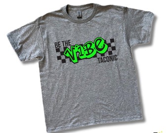 May include: A heather gray short-sleeve t-shirt featuring a black and neon green graphic print. The design includes a black checkered pattern, the text BE THE VIBE in neon green graffiti-style lettering, and the word TACONIC in black.